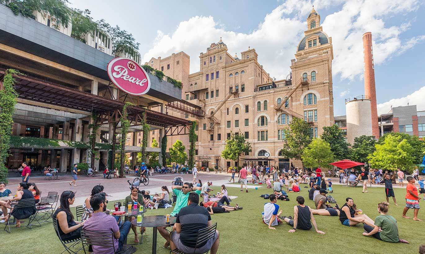 Groups of people occupy a large greenspace outside of Pearl Brewery in San Antonio, Texas.